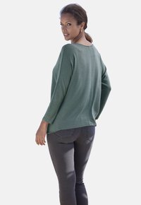 Grüner Pullover mit lässiger Passform, 3/4-Ärmeln und rundem Ausschnitt, kombiniert mit eng anliegenden, dunkelgrauen Jeans. Weicher Stoff.