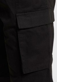 Black cargo pants feature a side pocket with a flap. Made from sturdy fabric, they have a straight cut and a smooth texture.