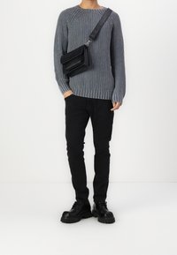 Šedý žebrovaný svetr s dlouhými rukávy, černé kalhoty a robustní černé boty. Malá černá crossbody taška dodává outfitu na detailech.