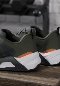 Paire de chaussures de sport vert foncé et noir avec des semelles blanches et des accents orange posées sur une surface en bois.