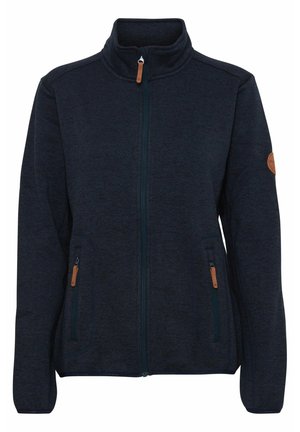 Granatowa polarowa kurtka z wysokim kołnierzem, przednim zamkiem błyskawicznym i dwiema kieszeniami na zamek. Ozdobiona brązowymi skórzanymi akcentami na zamkach błyskawicznych i rękawach.