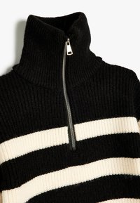 Pull à col zippé rayé noir et crème en tissu côtelé ; présente un col haut et un accent de fermeture éclair métallique.