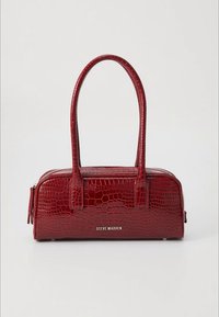Red crocodile-embossed handbag with two short handles, zip closure, and a silver "Steve Madden" logo on the front; smooth, glossy texture.