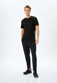 Camiseta deportiva negra de manga corta con detalles reflectantes, combinada con pantalones ajustados negros y zapatos negros sin cordones con detalles texturizados.
