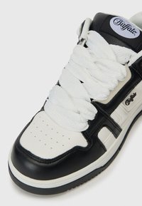 Crno-bijeli Buffalo tenisice s debelim bijelim vezicama, perforiranim prednjim dijelom, i crnom logotip oznakom na podstavljenom jezičku.