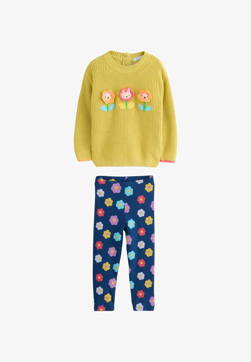 Pull en tricot jaune avec trois applications de fleurs en rose et bleu, associé à un legging marine avec des motifs floraux colorés.