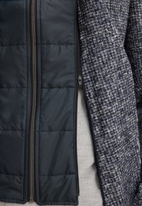 Gilet blu navy con texture trapuntata su un lato, tessuto intrecciato e strutturato sull'altro, con cerniera frontale e interno grigio.