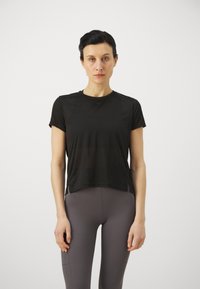 Svart kortermet treningstopp, lett materiale, rund halslinning, sidespalter. Kombinert med tettsittende, høyt liv grå leggings.