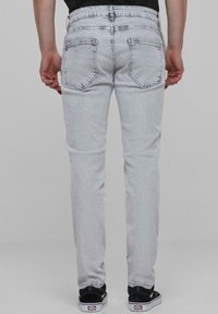Heledad hallid denim teksad, slim fit'i, viie taskuga ja nähtavate õmbluste detailidega, koos mustade tossudega.