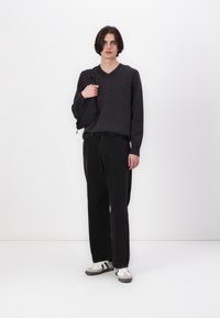 Grå v-hals genser, svarte løse bukser og grå joggesko med svarte striper. Modellen holder en svart crossbody-veske. Enkel, moderne stil.