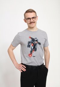 Camiseta de algodón gris con un gráfico de un superhéroe en armadura negra, con acentos rojos y el texto "Avengers" debajo del diseño.