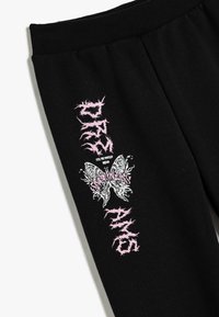 Schwarze Jogginghose mit einem gerippten Bund. Verziert mit einem pinken grafischen Text "DREAMS" und einem Schmetterlingsdesign.
