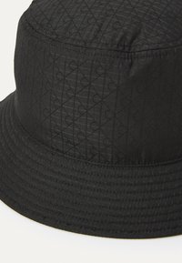 Cappello a secchiello nero con un motivo testurizzato di linee e forme intersecate. Tessuto morbido con un bordo cucito e design senza cuciture.