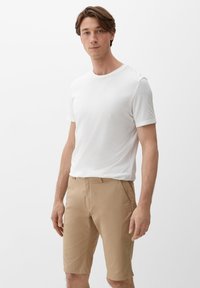 Witte T-shirt met korte mouwen gecombineerd met tan knielange shorts. Zacht katoenen stof, eenvoudig ontwerp en strakke lijnen. Geen patronen of accenten.