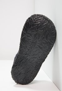 Schwarze Gummisohle mit strukturiertem, blattähnlichem Muster; der Rand ist abgerundet und erhöht. Der Hintergrund ist weiß und hebt das Design der Sohle hervor.