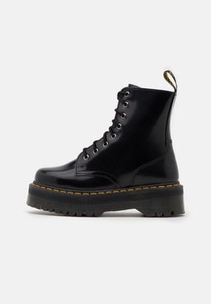 Czarne lakierowane botki na sznurowadła z grubą podeszwą, żółtym przeszyciem i pętelką z tyłu. Z metalowymi oczkami.