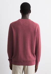 Maroon knit sweater with textured fabric, ribbed cuffs and hem, crew neckline, and seamless shoulder design. Viewed from the back.