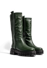 Bottes hautes en cuir vert foncé avec des semelles épaisses noires et robustes, bouts arrondis et languettes latérales, placées côte à côte sur un fond blanc.