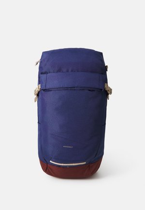 Backpack made of durable navy fabric with a brown bottom. Features a roll-top design, adjustable straps, and a small reflective strip at the base.