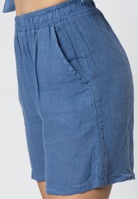 Pantaloni blu in lino con cintura elasticizzata, tasche laterali e una vestibilità allentata. La texture sembra morbida e leggermente stropicciata.