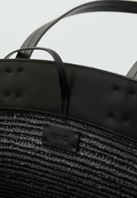 Borsa tote nera intrecciata con base testurizzata, dettagli in pelle liscia e un patch con il marchio. Presenta manici e sottili dettagli di cucitura.
