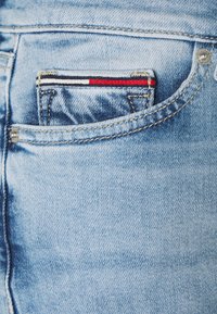 Jeans de mezclilla en un tono azul claro que presentan un pequeño bolsillo frontal con un patrón a rayas en rojo, blanco y azul, además de detalles de costura únicos.