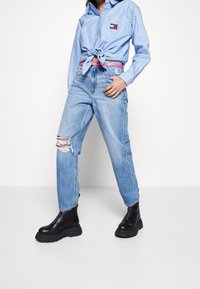 Light blue button-up shirt with a knotted front, paired with light blue ripped jeans and black chunky-sole ankle boots.