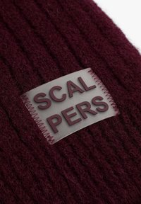 Tela de punto burdeos con una etiqueta de goma que dice "SCALPERS" en letras granate en relieve, acentuada con costuras contrastantes.