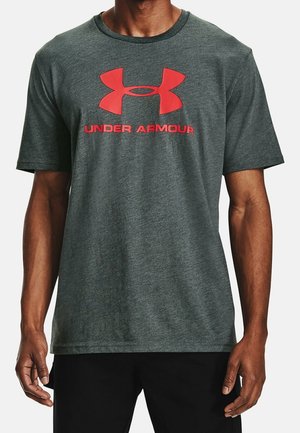 Man draagt een donkergrijs T-shirt met korte mouwen en een grote rode Under Armour-logo en tekst op de borst.