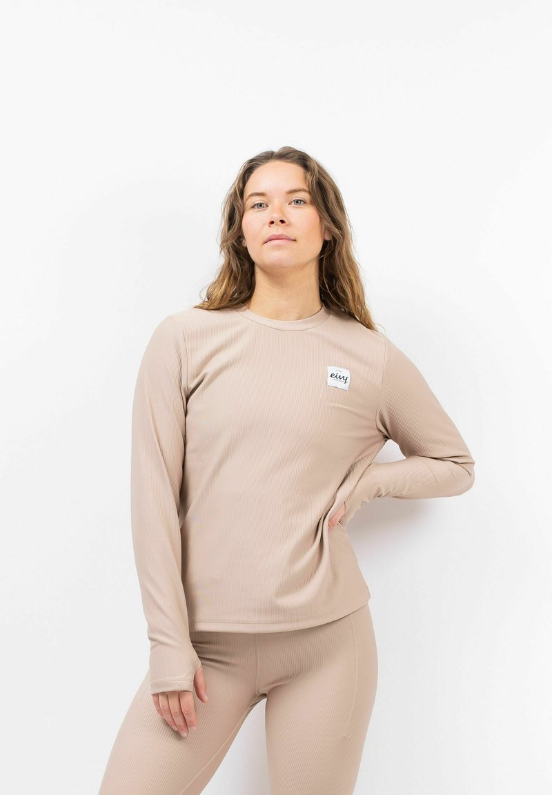 Langsleeve, beige sporttop van ribstof met een ronde hals. Bevat een klein, vierkant merkje op de bovenste linker borst.