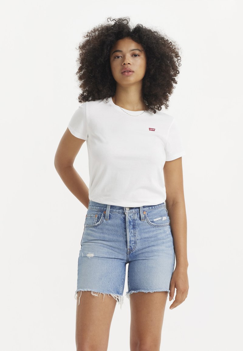 Valge lühikeste varrukatega T-särk punase Levi's logoga, millele on sobitatud heledat sinist teksapüksid, millel on kulunud serv ja kerged rebendid.