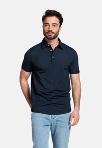 Polo shirt navy avec un col boutonné, des manches courtes et une texture lisse. Associé à un jean en denim bleu clair.