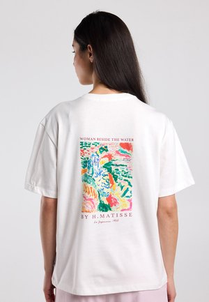 Woman wearing white t-shirt with colorful abstract painting and text "Woman Beside the Water by H. Matisse" on the back.