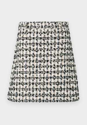 Austs pinums svārkos ar bēša un melna tvīda rakstu. Taisns siluets ar vieglu izvēršanos apakšmalā. Aprīkots ar jostasvietu un pogas detaļu.