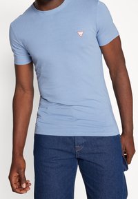 Lyseblå kortærmet t-shirt lavet af bomuld med et tætsiddende design. Har et lille trekantet rødt logo på venstre bryst.