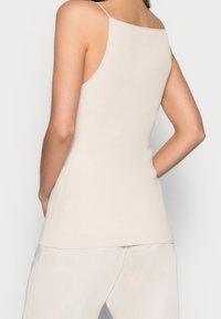 Top a costine, senza maniche, di un beige chiaro con un design aderente. Presenta spalline sottili e una schiena a taglio dritto, realizzato in un materiale morbido.