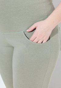 Světle zelené legíny vyrobené z měkké látky, s boční kapsou a hladkou texturou s precizním prošíváním podél švů.