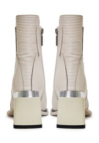 Bottes chevilles en cuir beige avec des rainures verticales, accent argenté au talon, bout carré et fermetures éclair latérales. Base épaisse et contrastante.