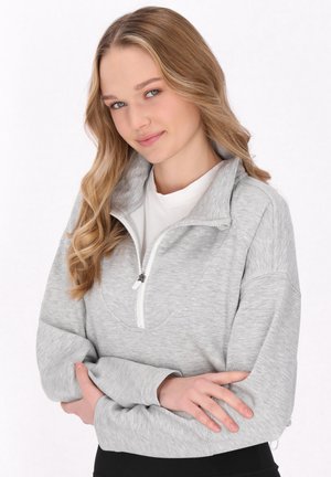 Grå zip-up sweatshirt med høj krave og blød tekstur. Har en hvid lynlås og dropped shoulders. Bæres med en hvid t-shirt under.
