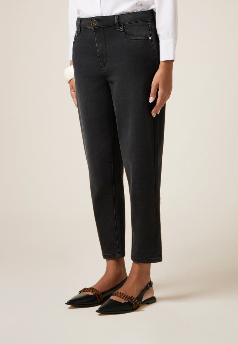 Pantalones de mezclilla negros con un ajuste slim, que presentan un diseño de cinco bolsillos, cierre de botón y dobladillos enrollados. Combinados con zapatos planos negros puntiagudos y una blusa blanca.