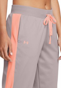 Gaišas pelēkas sporta bikses ar elastīgu jostasvietu un korallkrāsas sānu svītrām. Ar šnūrīšu aizdari un mazu логотипu tuvu kabatai.