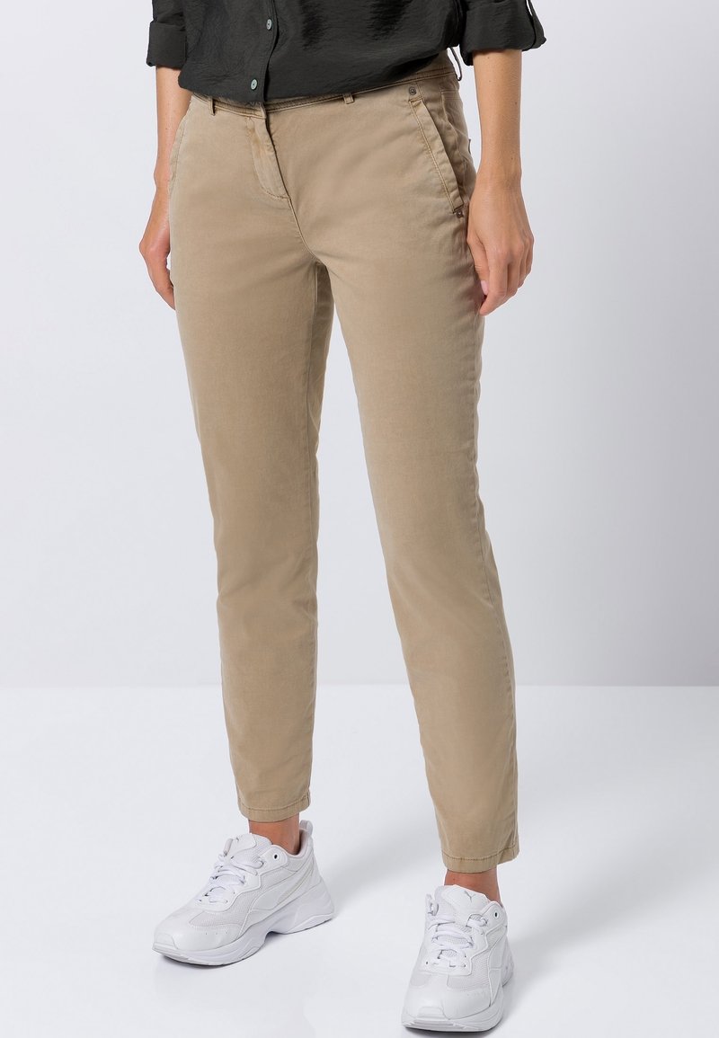 Pantalons en coton beige à coupe slim, avec une fermeture à bouton et zip, des poches avant et des ourlets retroussés, associés à des baskets blanches.