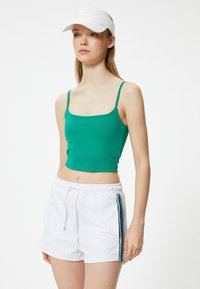 Top corto verde ajustado con tirantes finos, combinado con shorts blancos que tienen rayas azules y verdes a los lados. Tejido ligero.