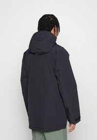 Dunkelblaue wasserdichte Jacke mit Kapuze, mit glatter Oberfläche, leicht oversized Design und verstellbaren Bündchen. Keine sichtbaren Logos.