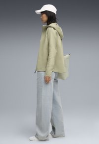 Felpa verde chiaro con cappuccio, vestibilità comoda, abbinata a jeans larghi azzurri, sneakers bianche e cappellino bianco.