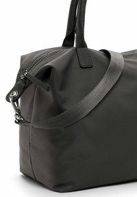 Zwarte nylon tas met een gladde textuur; voorzien van een lange verstelbare riem, korte handvatten en een metalen rits met trekker. Accenten met matte afwerking.