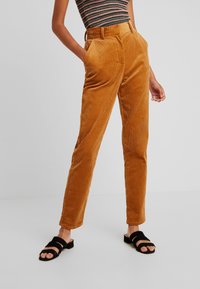 Kabelbyxor i varm orange-brun med texturerade ränder, midjehöjd i normal höjd, sidofickor och smalnande ben. Parades med svarta halksandaler.