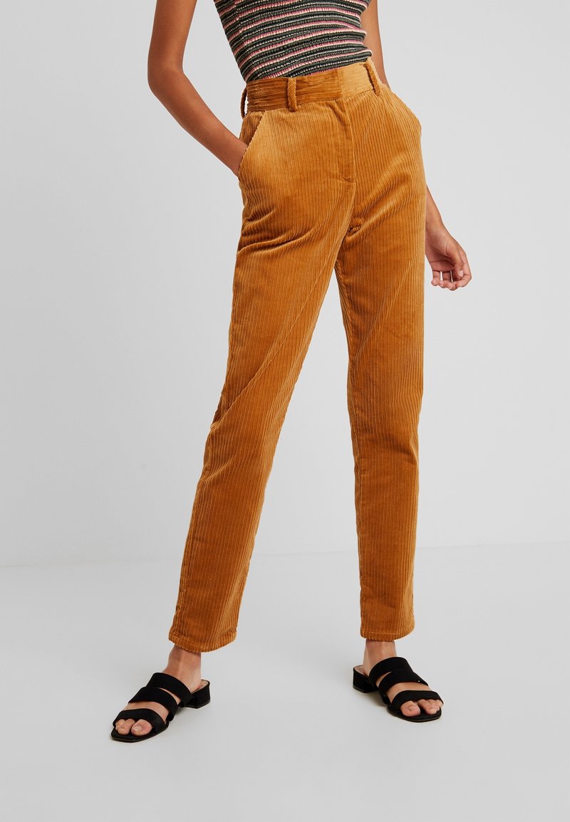 Kabelbyxor i varm orange-brun med texturerade ränder, midjehöjd i normal höjd, sidofickor och smalnande ben. Parades med svarta halksandaler.