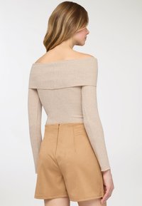 Top beige a coste con scollo a barca abbinato a pantaloncini coccio morbidi e a vita alta, con una cerniera nascosta sul retro.