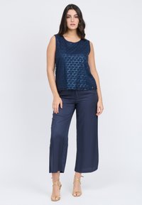 Top senza maniche blu navy con motivo esagonale testurizzato, abbinato a pantaloni larghi in satin scuro e sandali con tacco dorati.